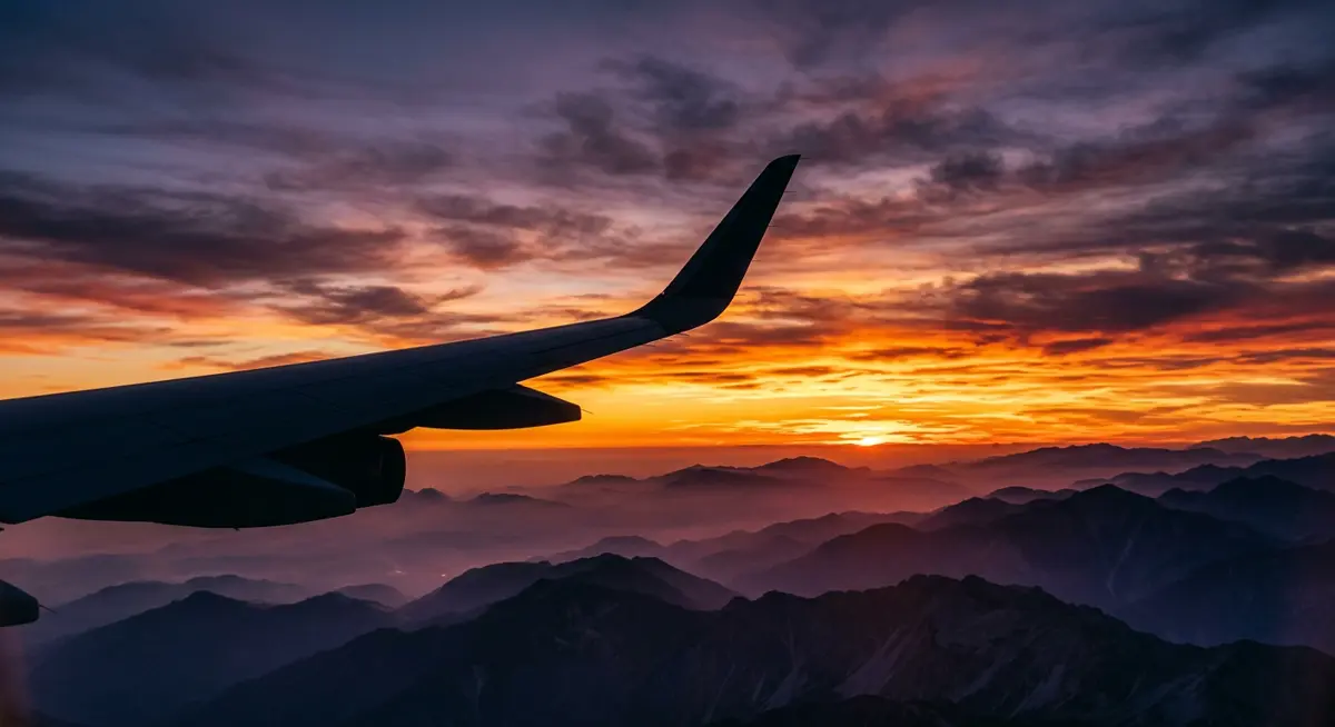 Airplane wing silhouetted against a sunset over mountain ridgelines
